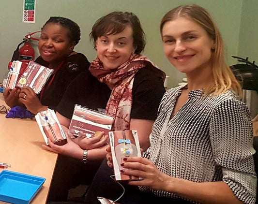 Three women holding packages in a room VeinTrain flat-pack vein simulator for phlebotomy and cannulation training