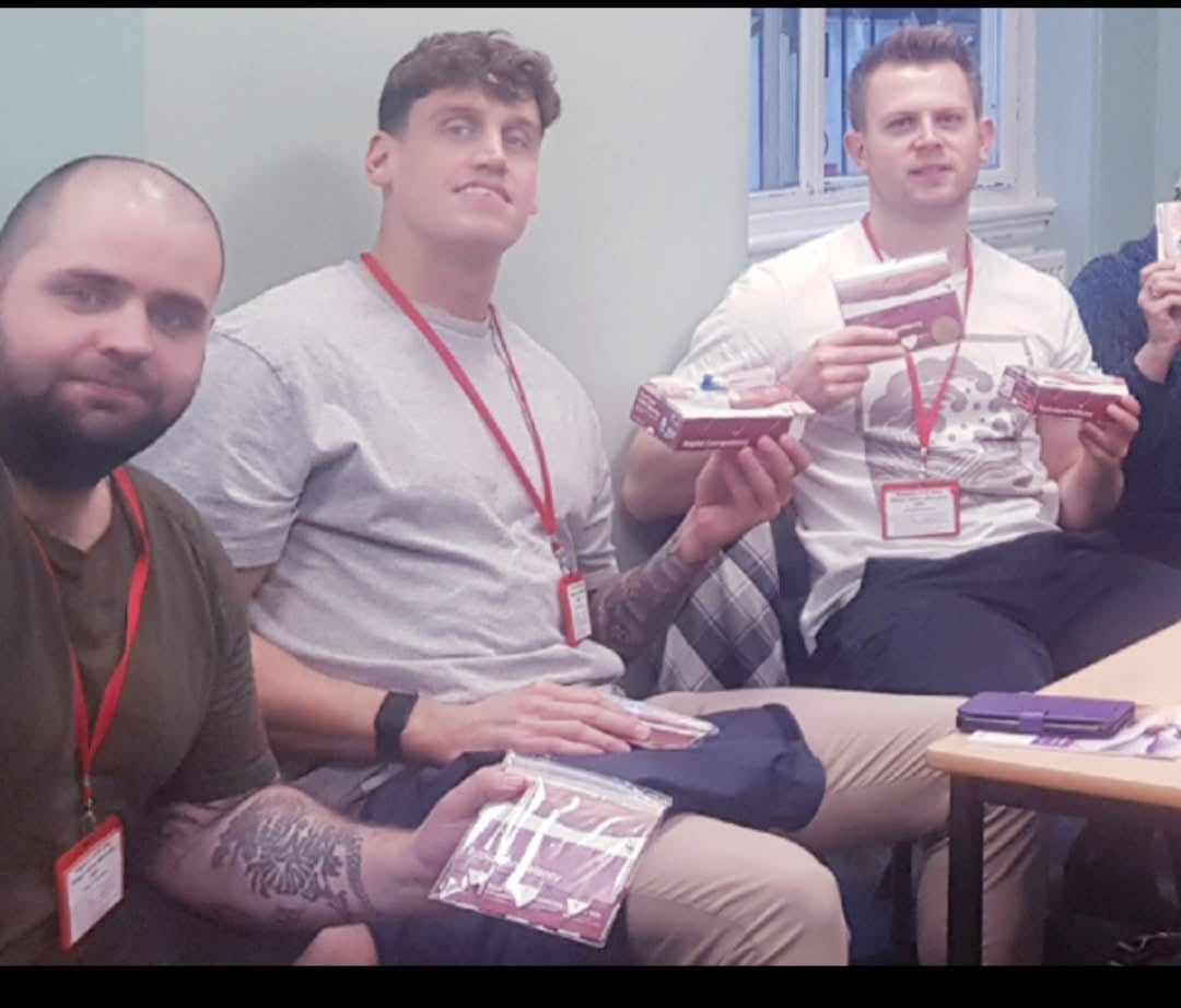 Three men sitting together, two of whom are holding packages.  VeinTrain flat-pack vein simulator for phlebotomy and cannulation training
