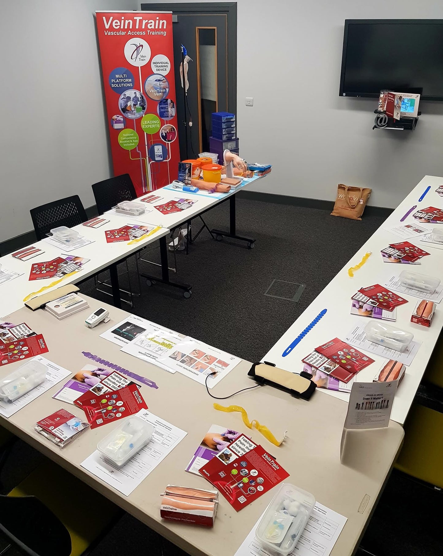 Meeting room with tables covered in promotional materials and a VeinTrain banner.  VeinTrain flat-pack vein simulator for phlebotomy and cannulation training
