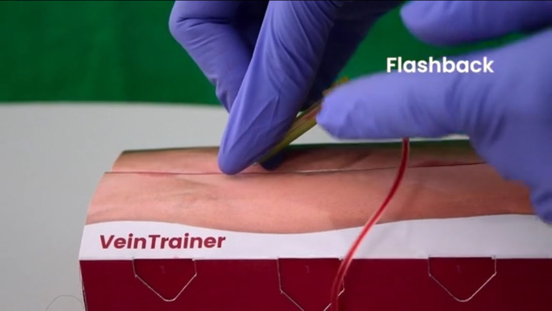 Gloved hand using a vein trainer on a mannequin arm with 'VeinTrainer' branding. VeinTrain flat-pack vein simulator for phlebotomy and cannulation training
